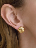 Gold shell-shaped earring worn by a person with long hair.