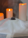 A small dark crystal cluster rests on a white cloth in the foreground, with blurred white candles glowing in the background.