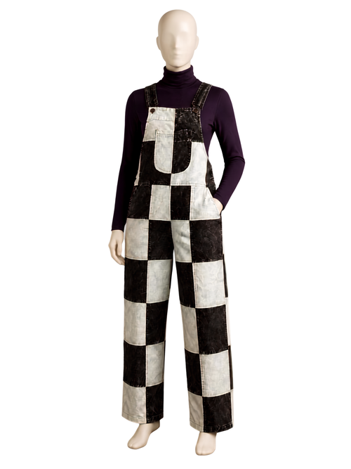 A mannequin wearing a black and off-white checkered patchwork overall jumpsuit over a dark purple long-sleeve turtleneck, shown against a plain white background.