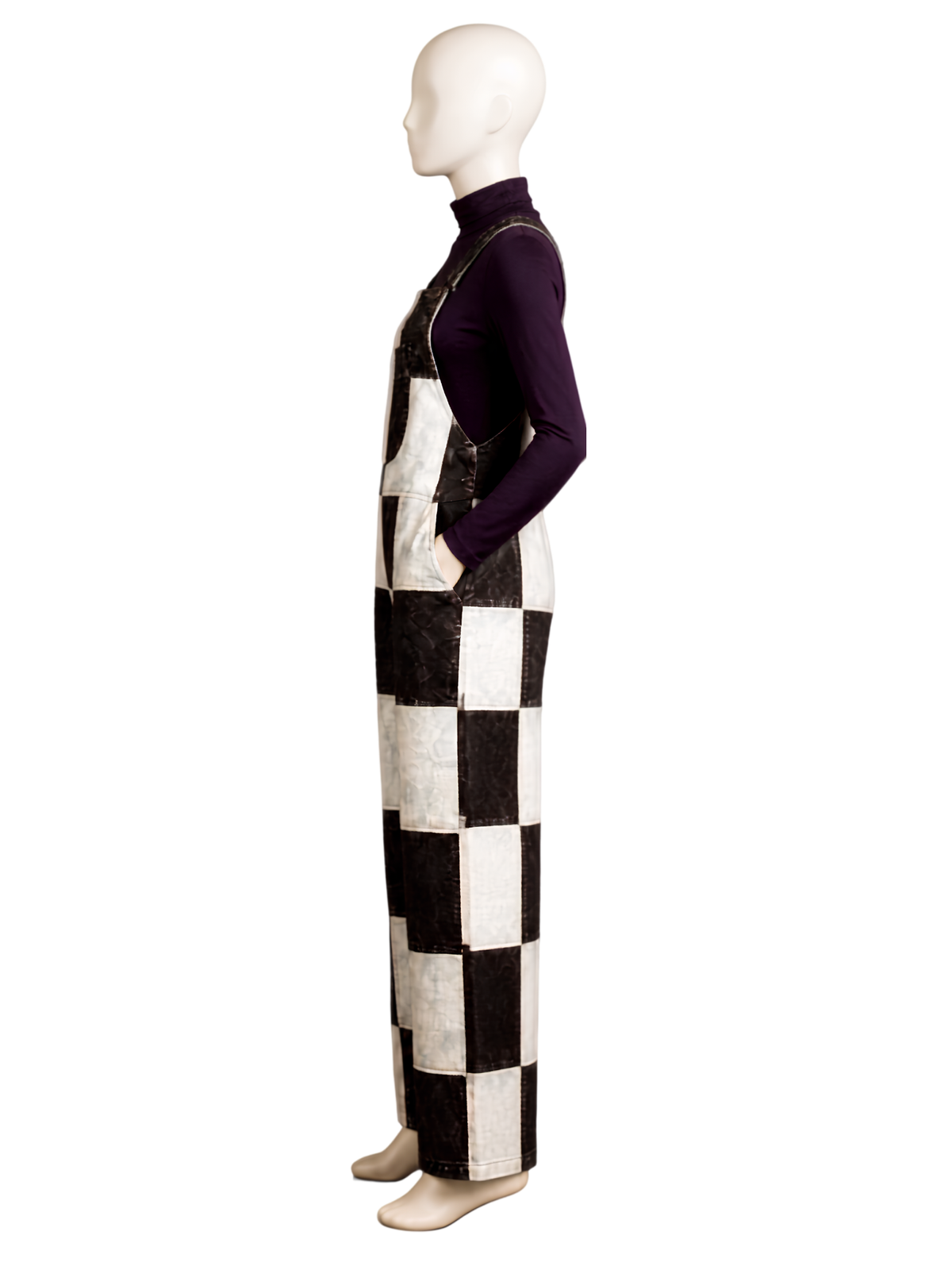 A mannequin wearing a long-sleeve dark purple turtleneck and black-and-white checkered bib overalls, shown in side profile against a plain white background.