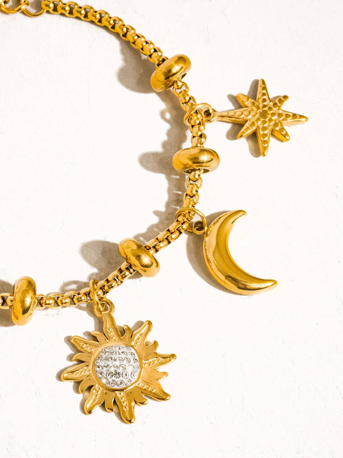 Gold bracelet with sun, moon, and star charms on a white background